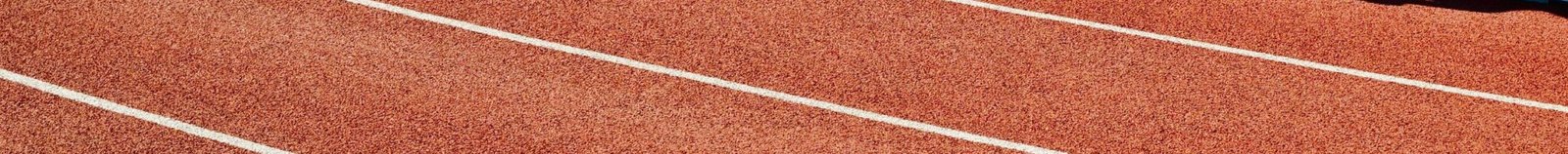 Athlete running on a red track in an outdoor stadium on a sunny day.